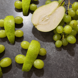 Kleine Rennautos aus Birne und Weintrauben mit Obst daneben